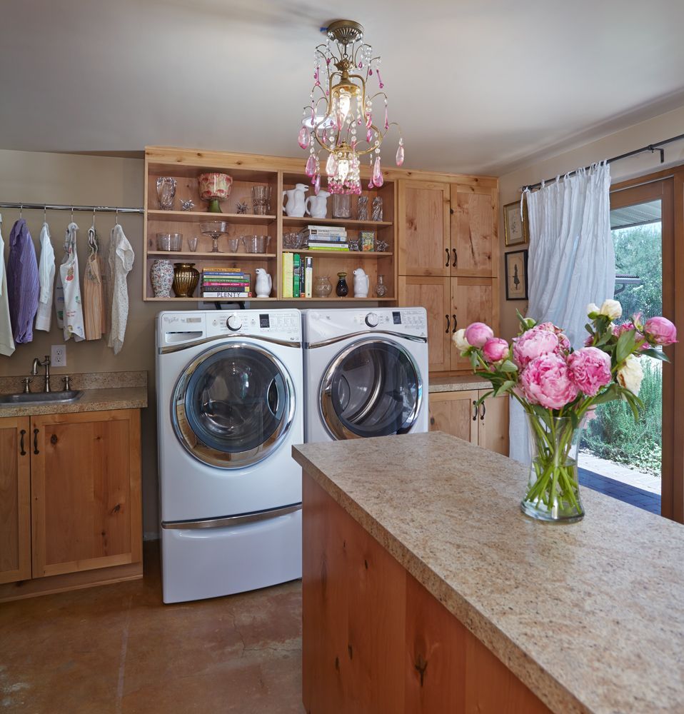 Laundry room with washer, dryer, counter, and a chandelier. A clothes rack is on the left. A vase of pink flowers on the counter.