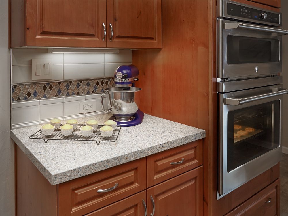 Kitchen counter with cupcakes, mixer, and built-in oven. Cabinets are brown.