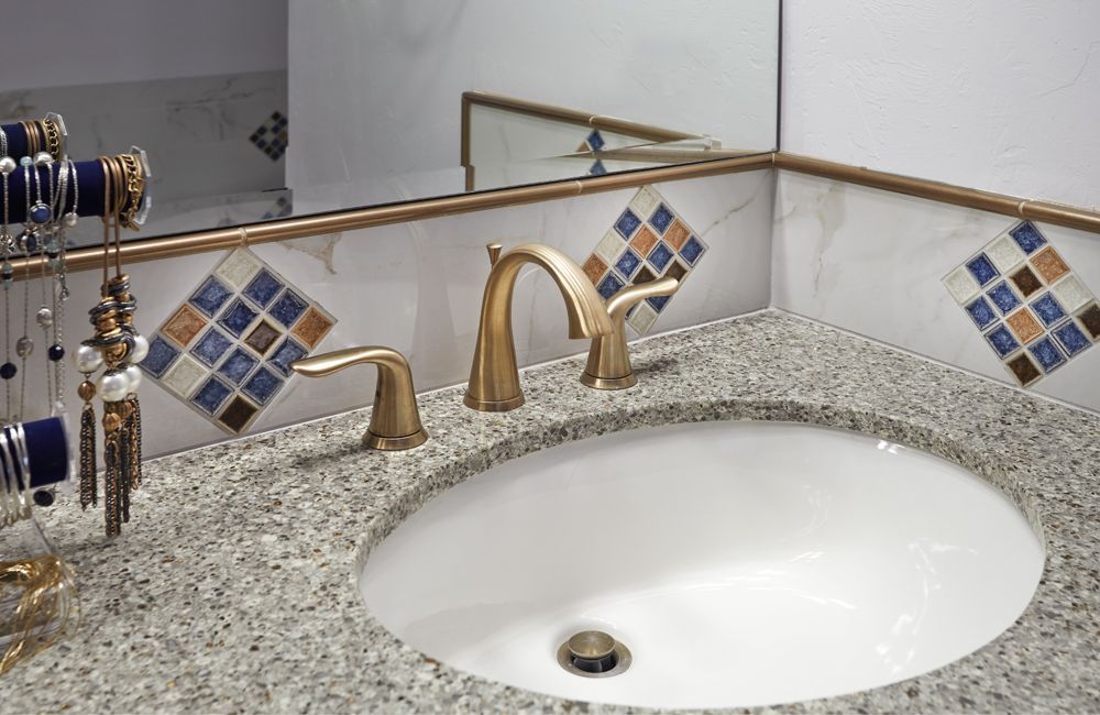 Bathroom sink with gold faucet, granite countertop, and tiled backsplash.