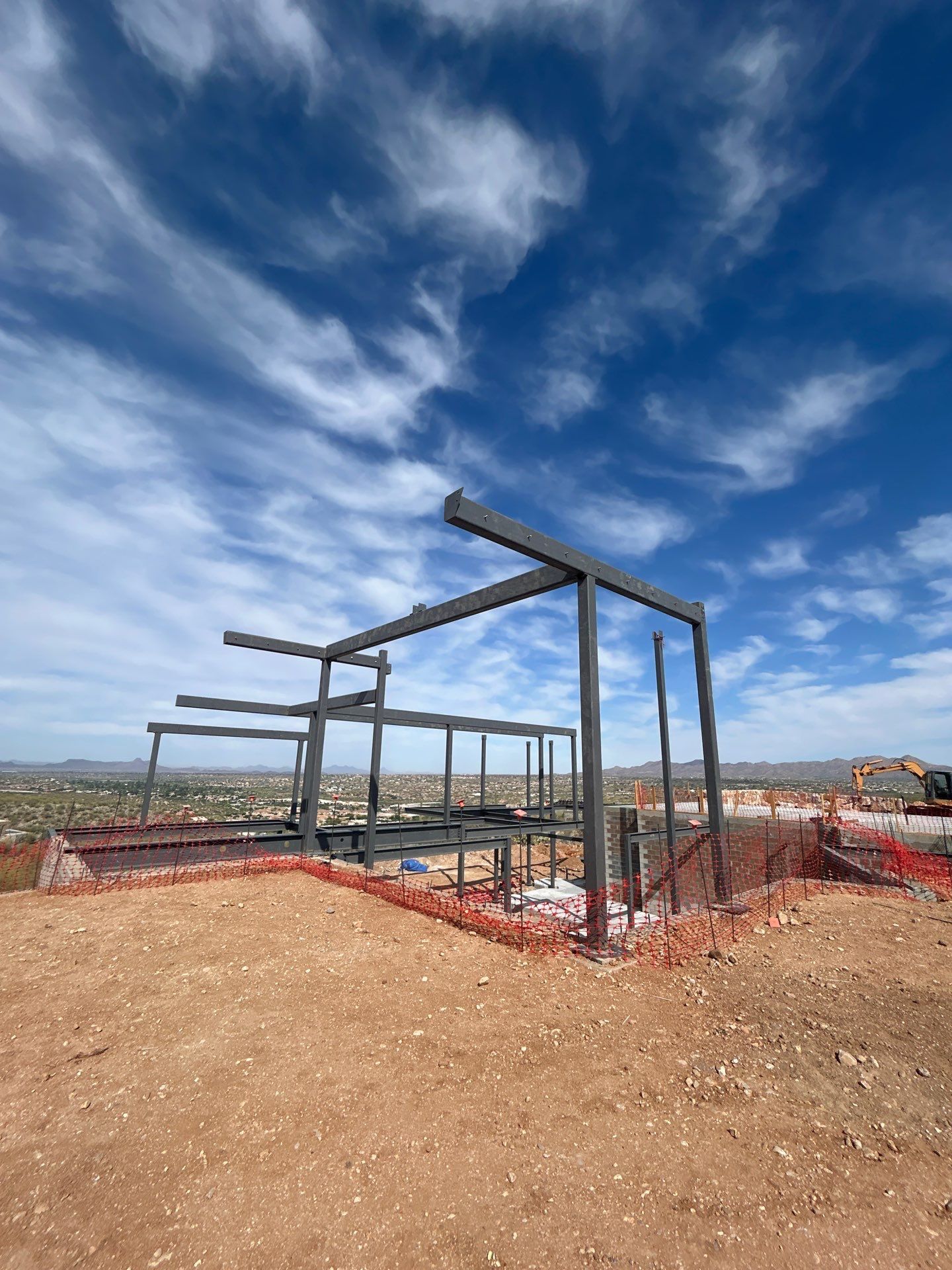 Construction site: Steel frame of a building against a blue sky with scattered clouds.
