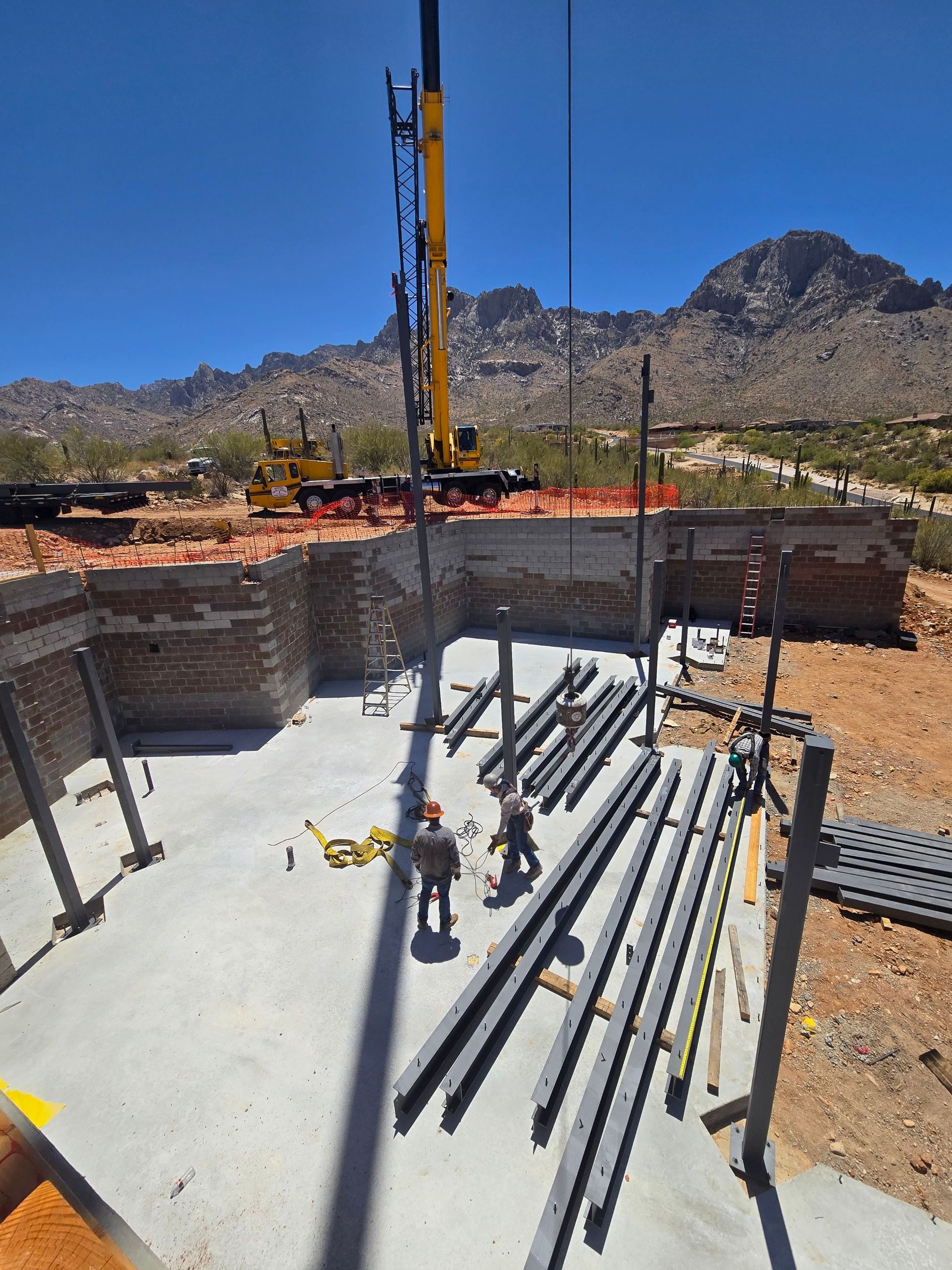 Construction workers installing steel beams with a crane at a building site in a desert landscape.