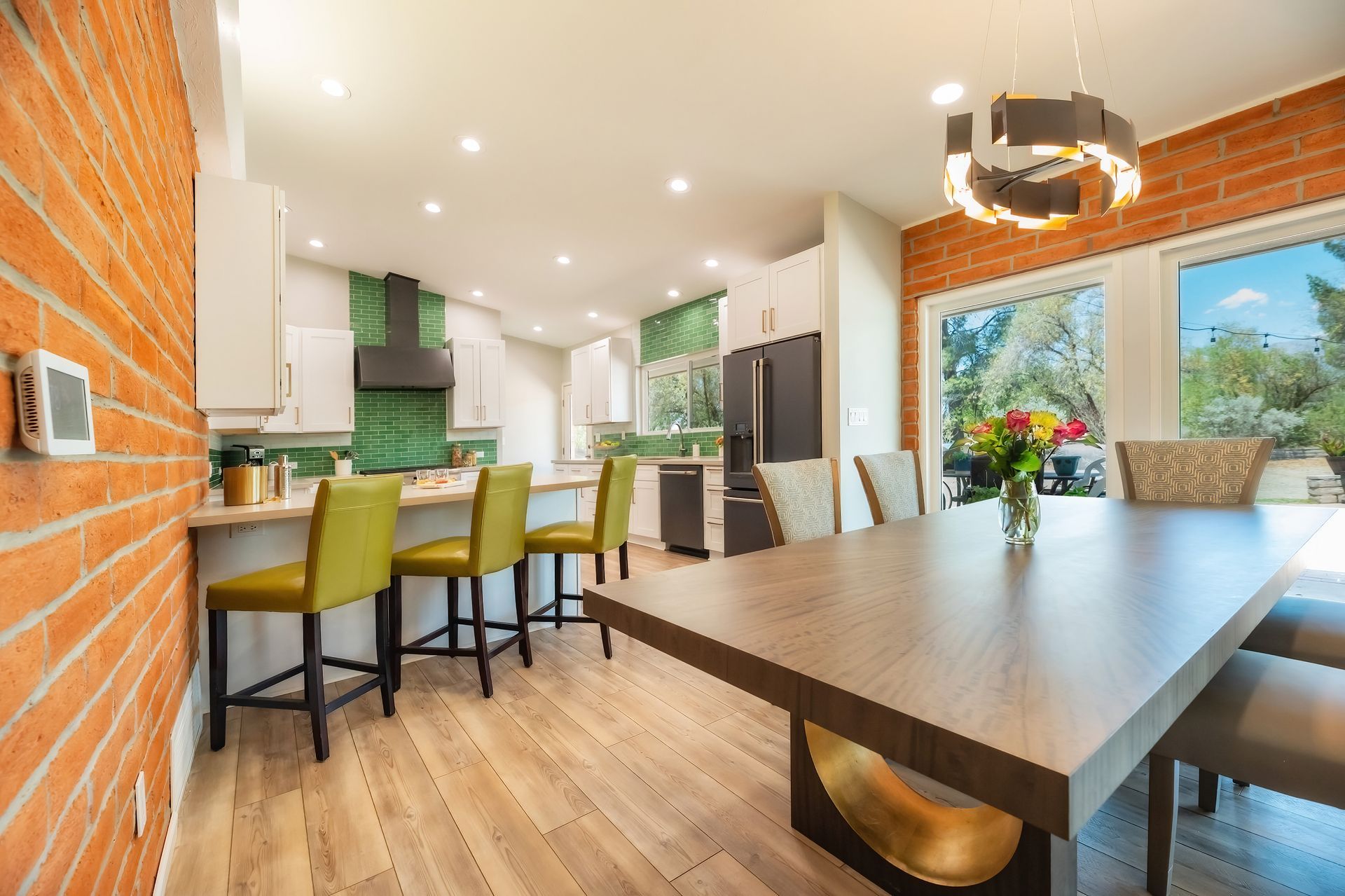 Modern kitchen and dining room with exposed brick, green tile, and a long wooden table.
