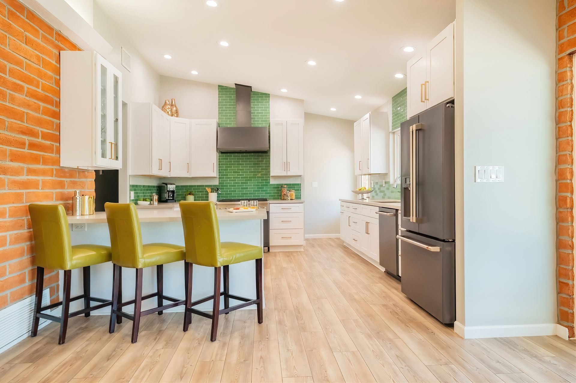 Modern kitchen with brick wall, white cabinets, green backsplash, and yellow bar stools.