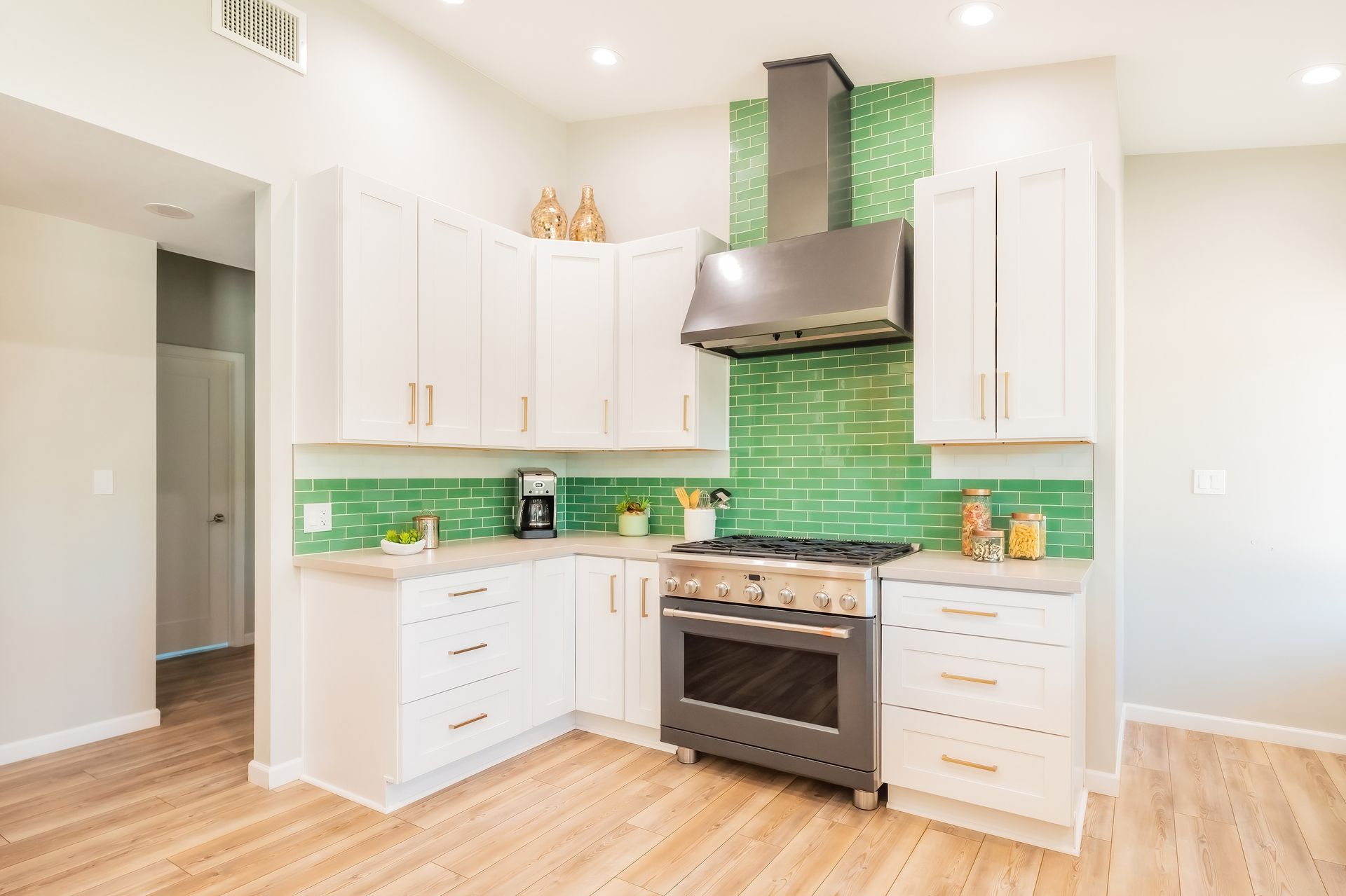 White kitchen with green backsplash, stainless steel appliances, and light wood flooring.