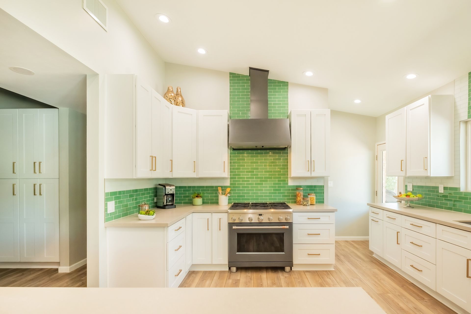 A kitchen with white cabinets and green tiles on the walls.