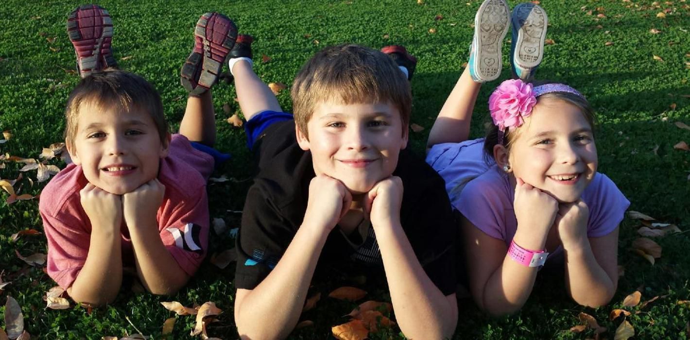 Children lying on grass with hands under their chins.