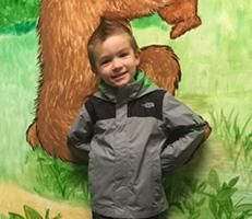 A young boy is standing in front of a painting of a bear.