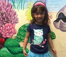 A little girl is standing in front of a painting of a turtle and coral reef.