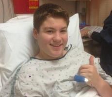 A young boy is giving a thumbs up while laying in a hospital bed.