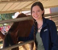 A woman is standing next to a horse behind a fence.