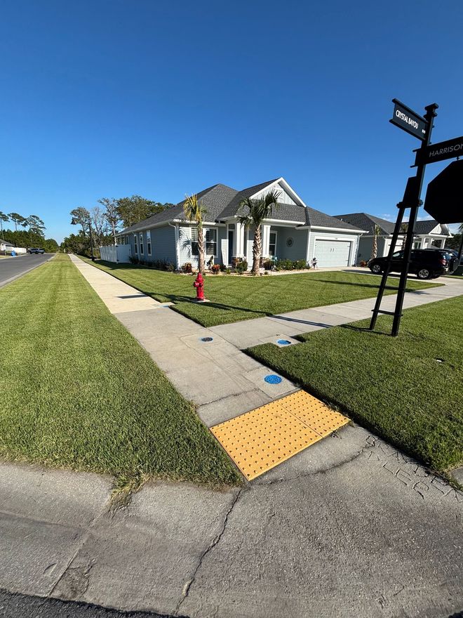 Green lawn with a concrete walkway. Buildings in the background, a lawnmower in the middle, and bushes to the right.