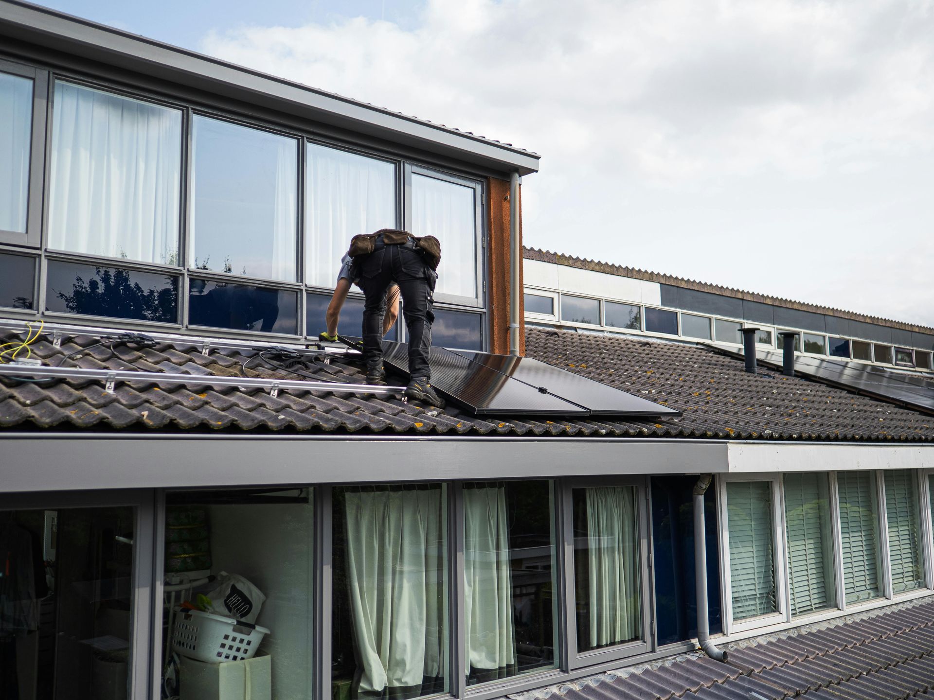 Person installing solar panels on a rooftop with multiple windows below.