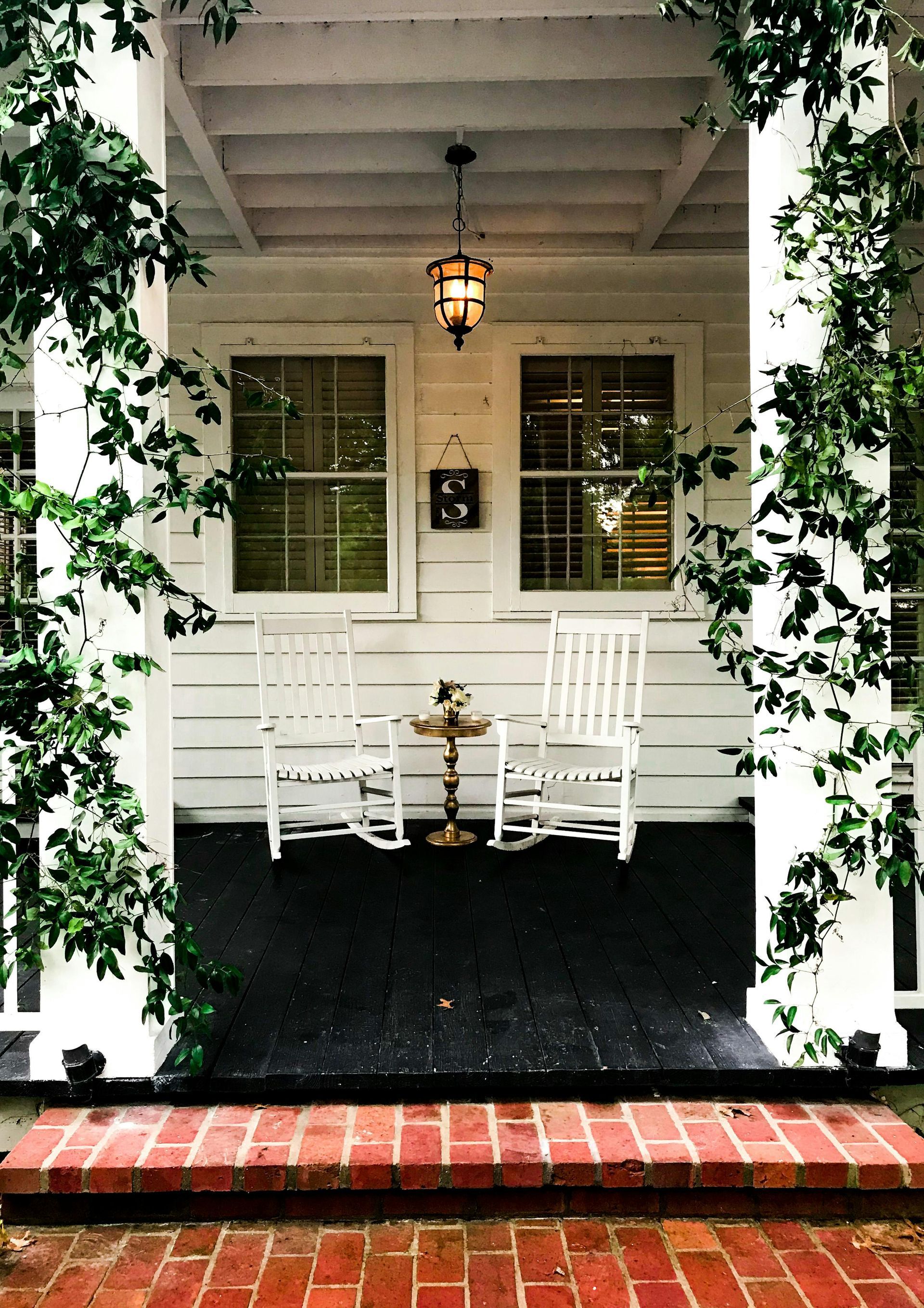 White porch with rocking chairs, brick steps, and ivy.