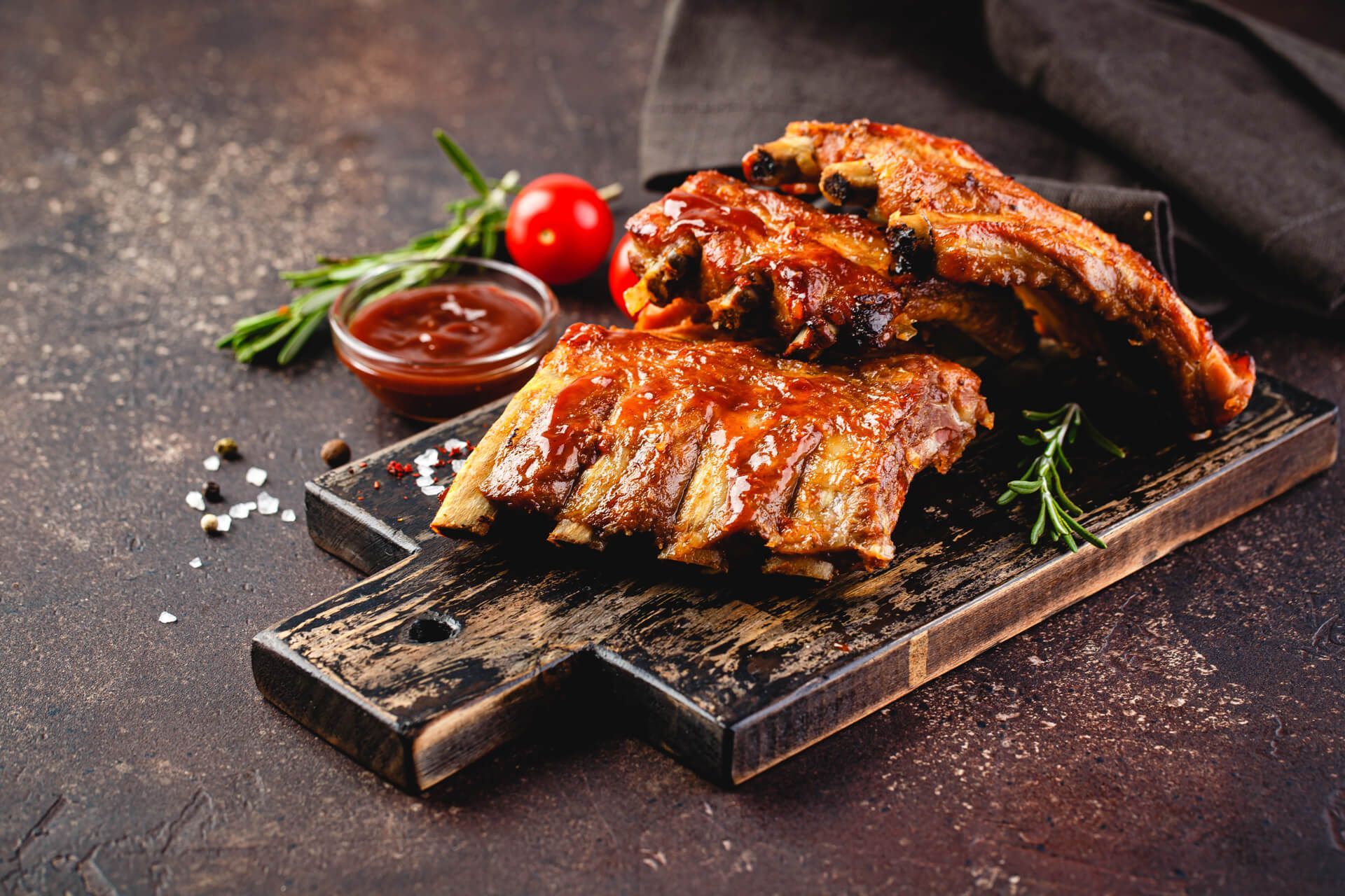 Grilled pork ribs on a wooden cutting board with sauce and tomatoes