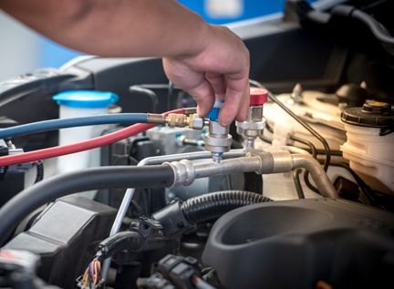 A technician connects blue and red hoses to a car engine's air conditioning system for maintenance.