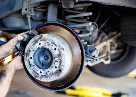 A mechanic's hands are working on a car's brake rotor. Close-up shot shows the wheel and suspension system.