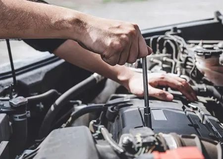 Hands using a wrench to repair a car engine in an open hood compartment