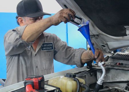 A man is pouring oil into a car through a funnel.