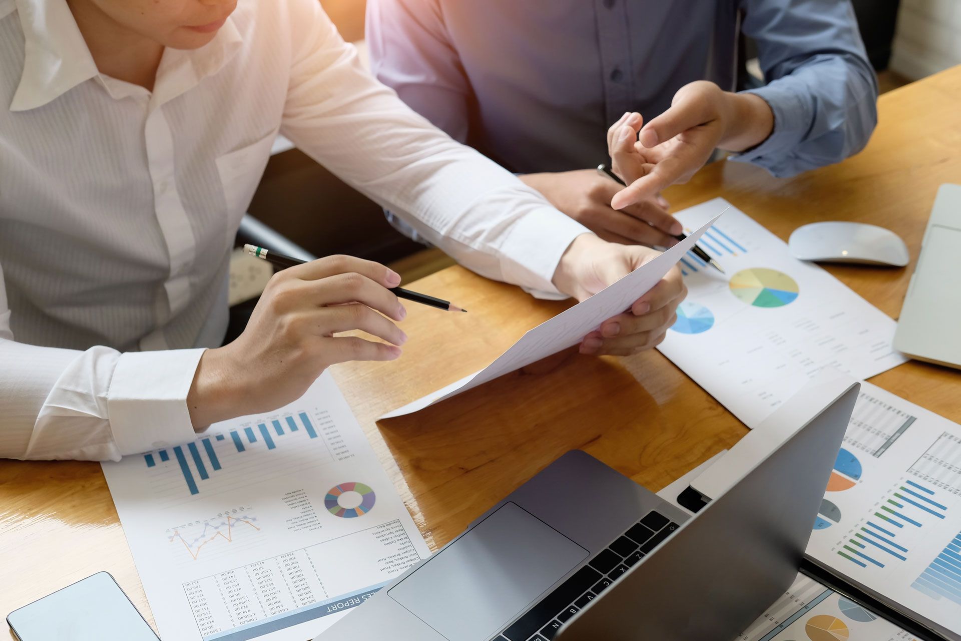 Two people in business shirts reviewing documents and charts at a table with a laptop.