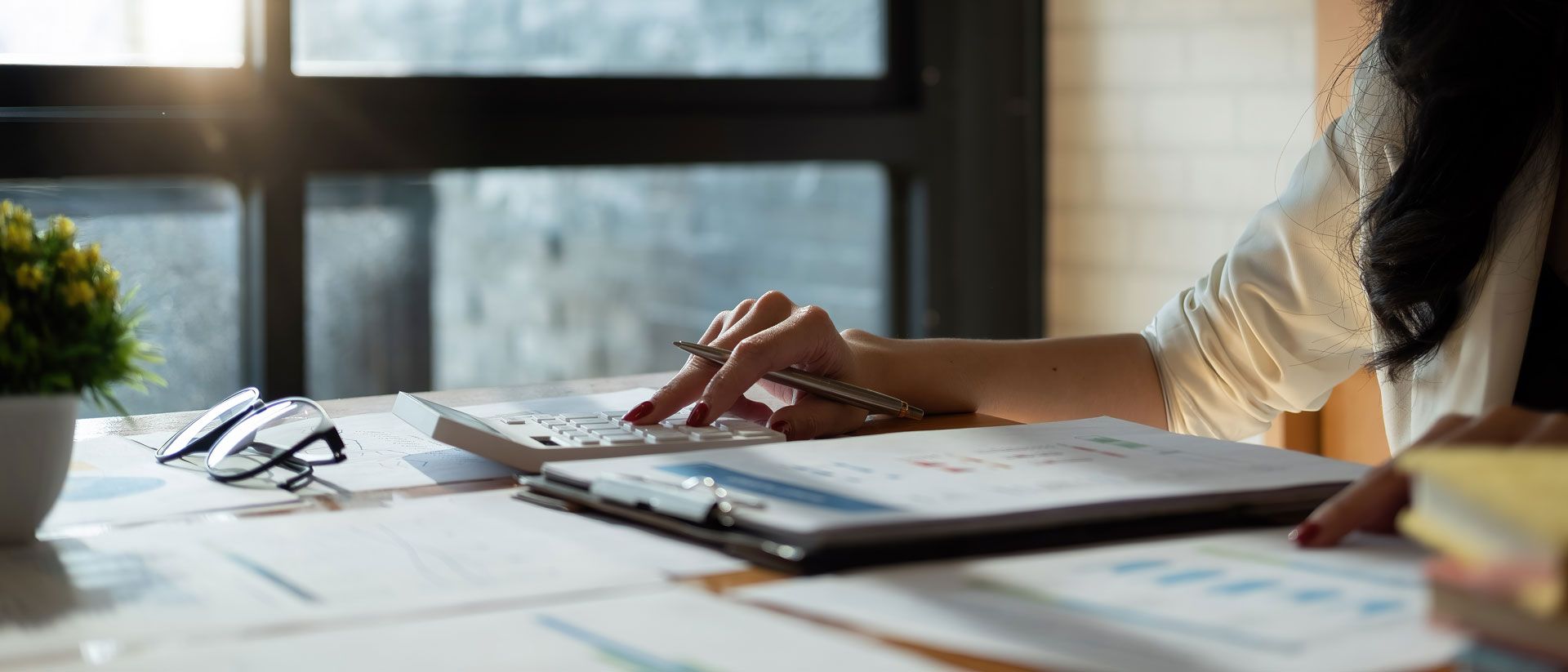 Person using a calculator while working on paperwork at a desk.