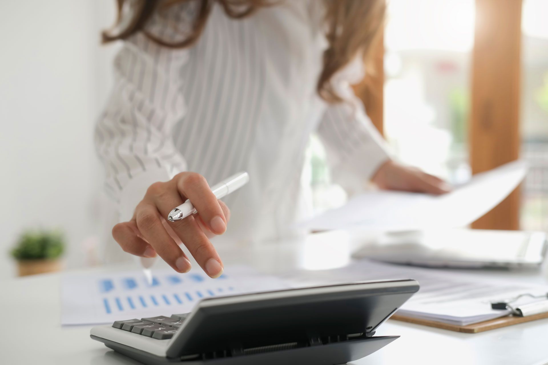 Person using a calculator, holding a pen, reviewing documents, and working in an office setting.