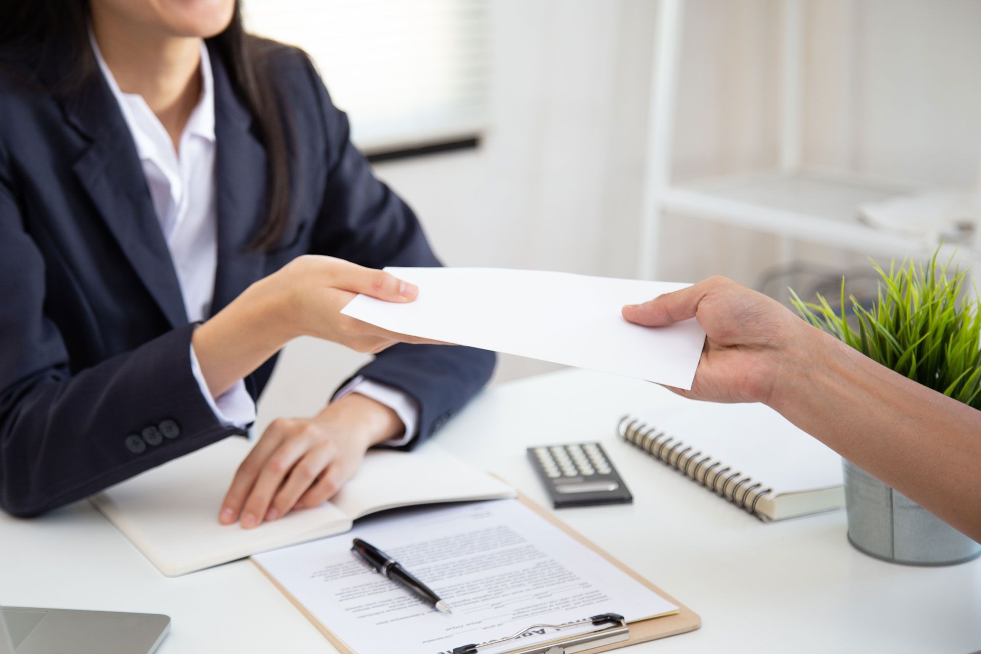Person in blazer passing document to another person at a desk.