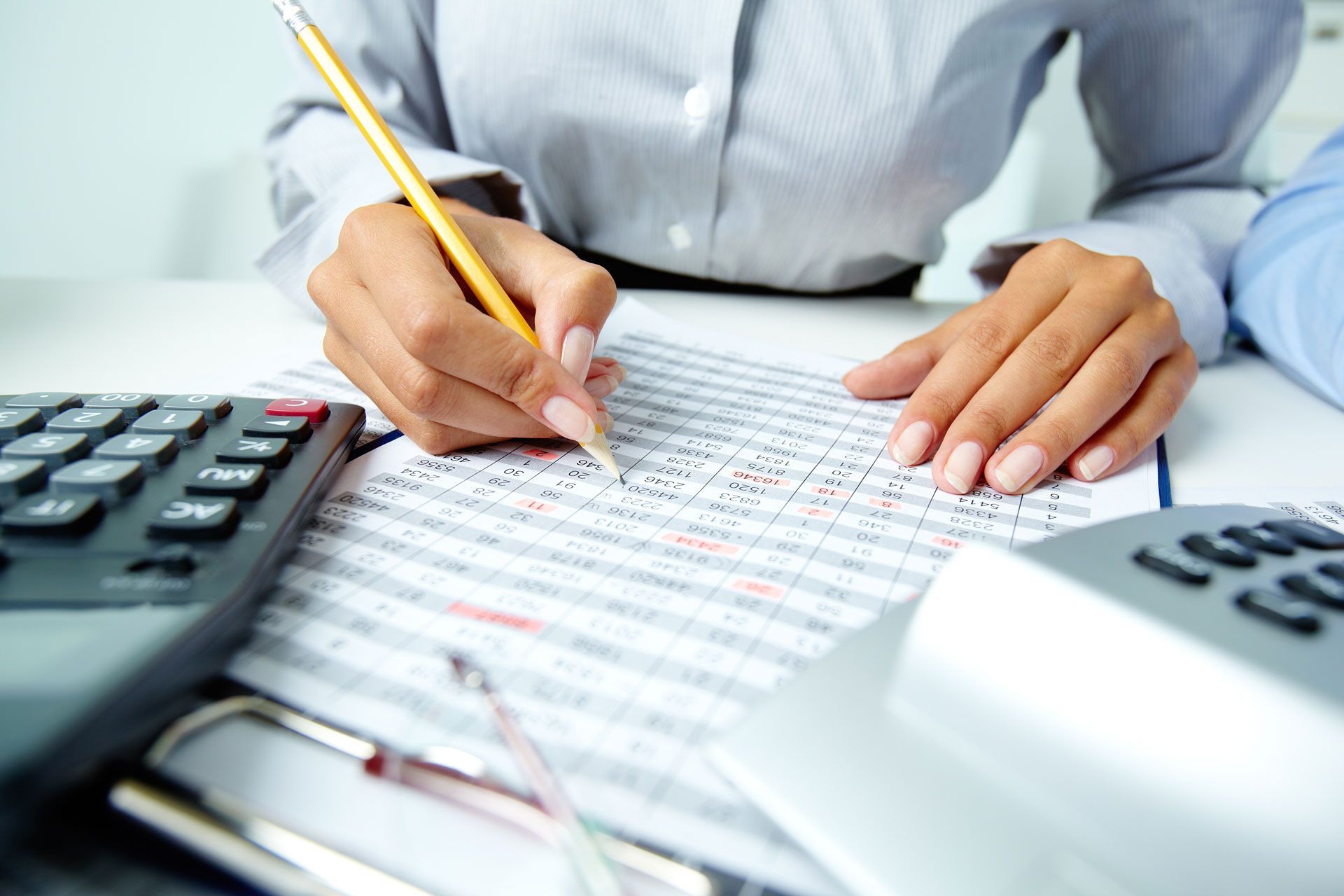 Person writing with a pencil on a ledger, next to a calculator and phone.
