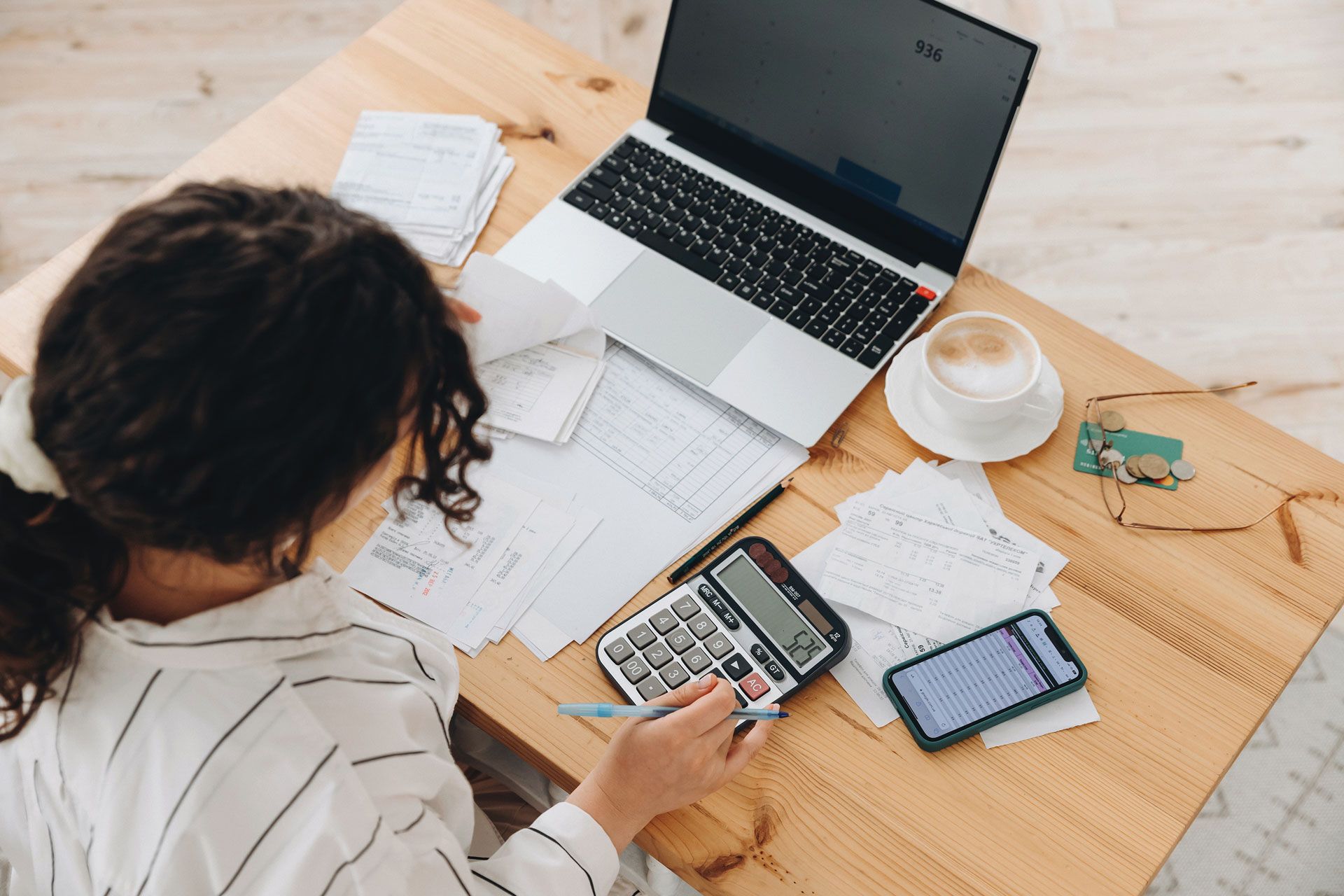 Woman working at a desk with laptop, calculator, and papers, calculating finances.