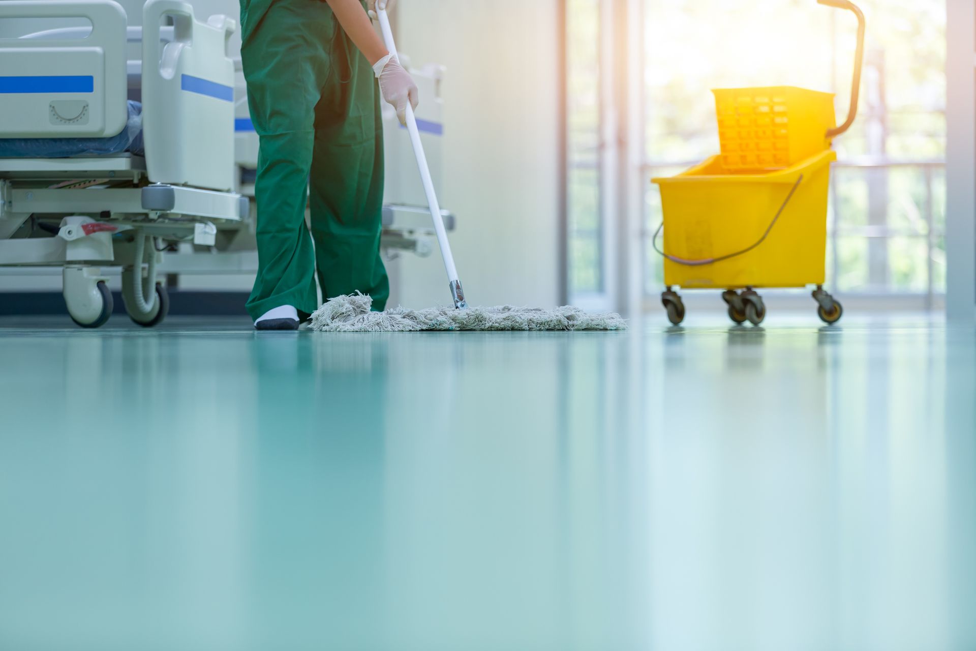 A nurse is cleaning the floor of a hospital with a mop.