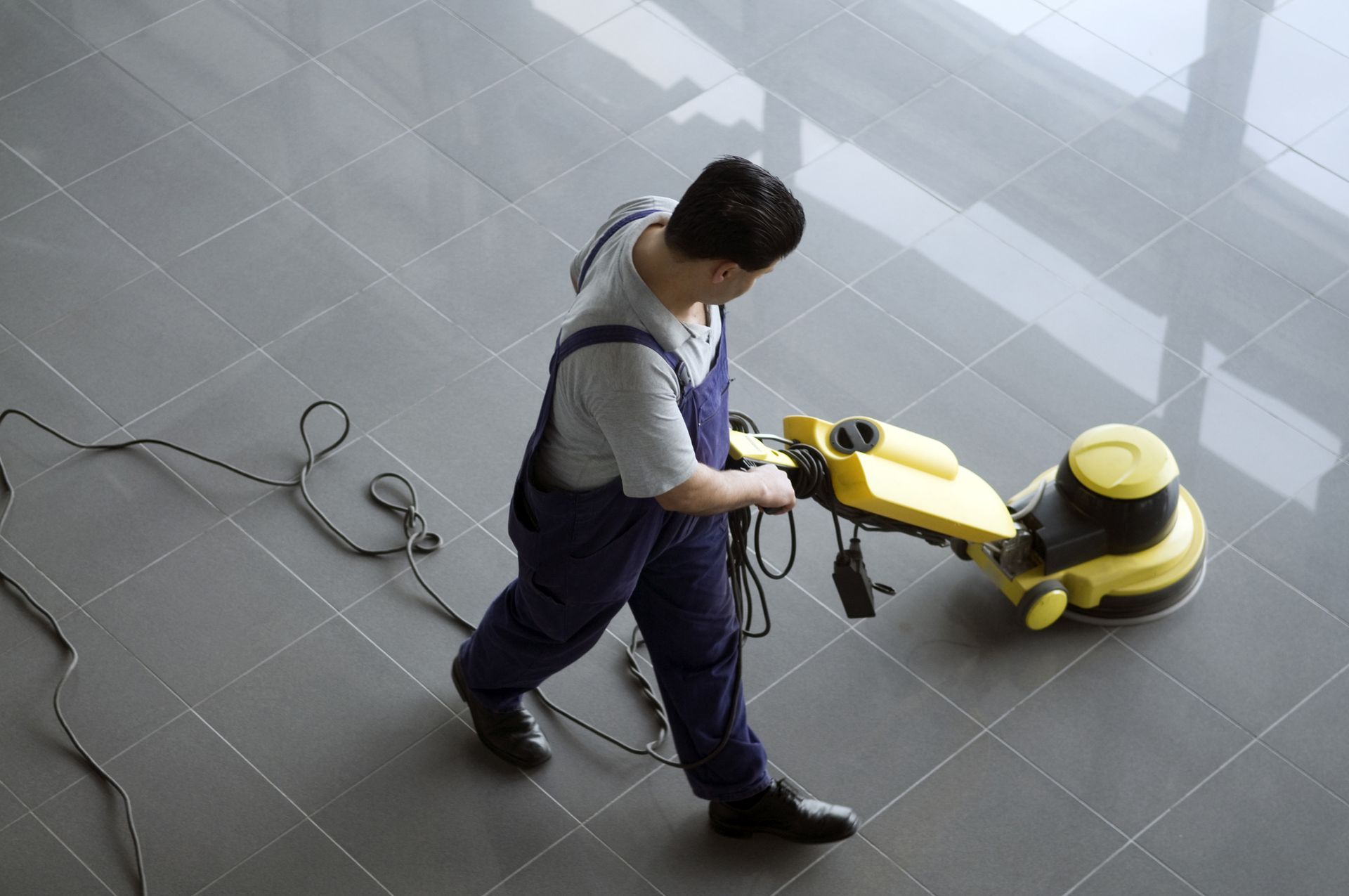 A man is cleaning a tiled floor with a machine.