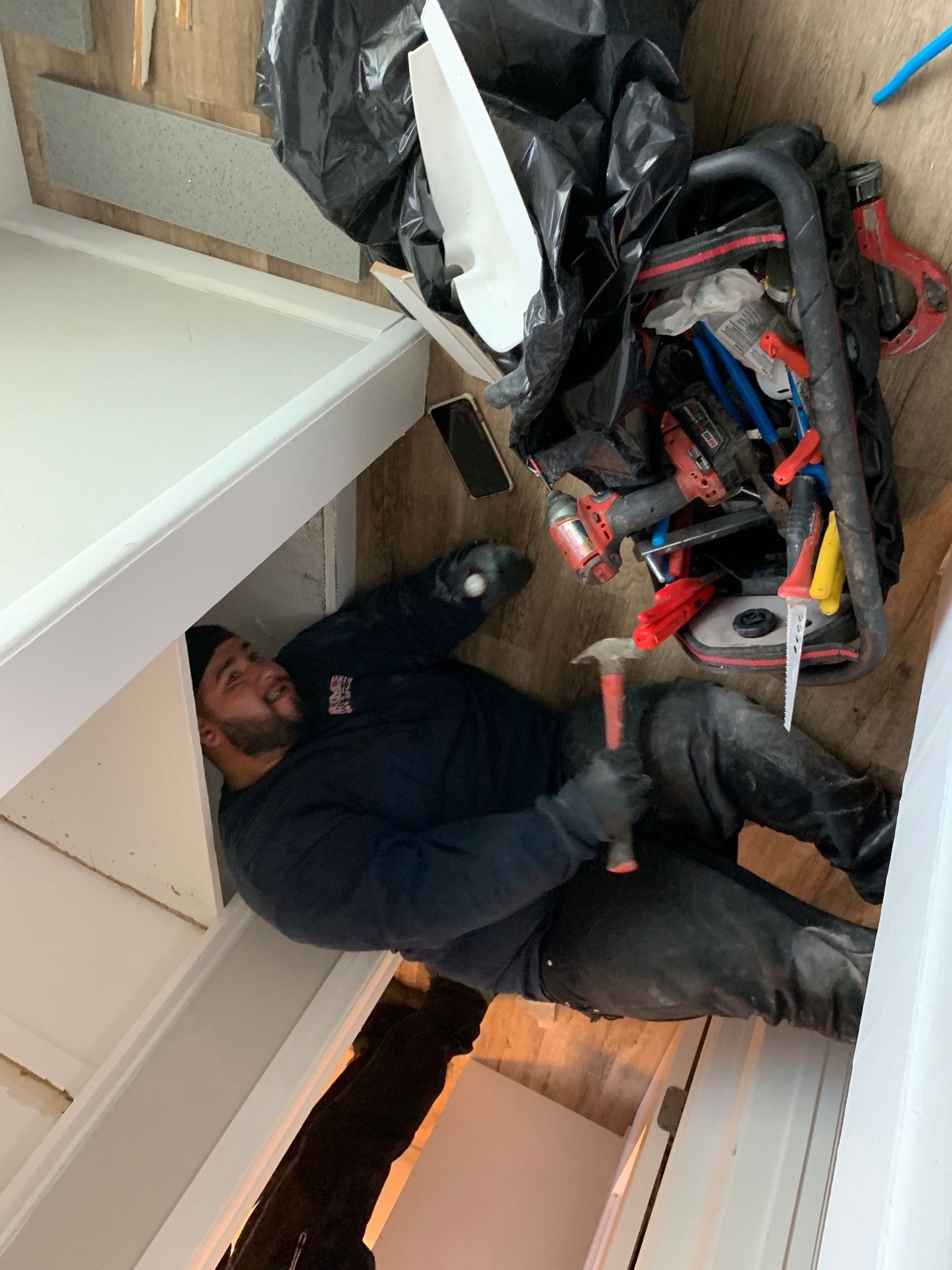 Man working on floor, holding a hammer, surrounded by tools and construction materials.