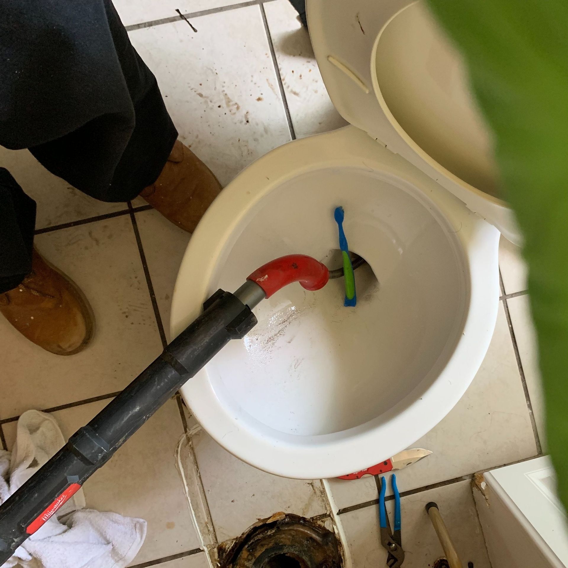 Plumber unclogging a toilet. A vacuum hose is inserted, with a toothbrush visible inside the bowl.