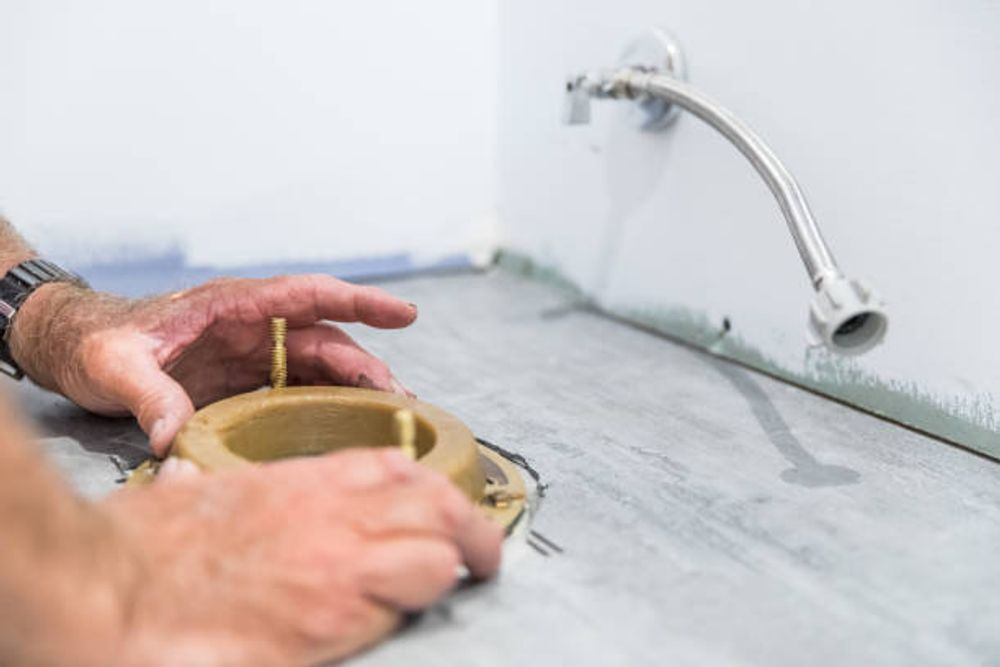 A person installs a wax toilet seal on a bathroom floor.
