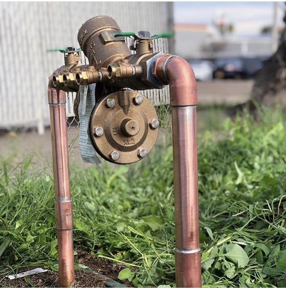 Copper pipes and a valve assembly outdoors in grass.