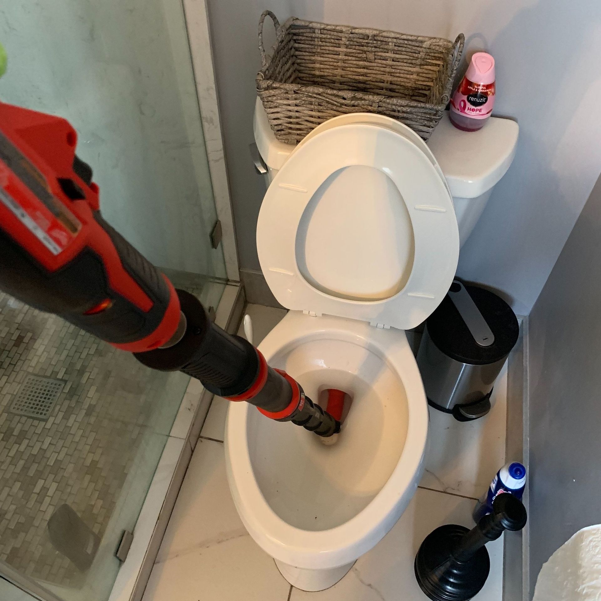 A person uses a red and black tool to unclog a toilet in a bathroom.