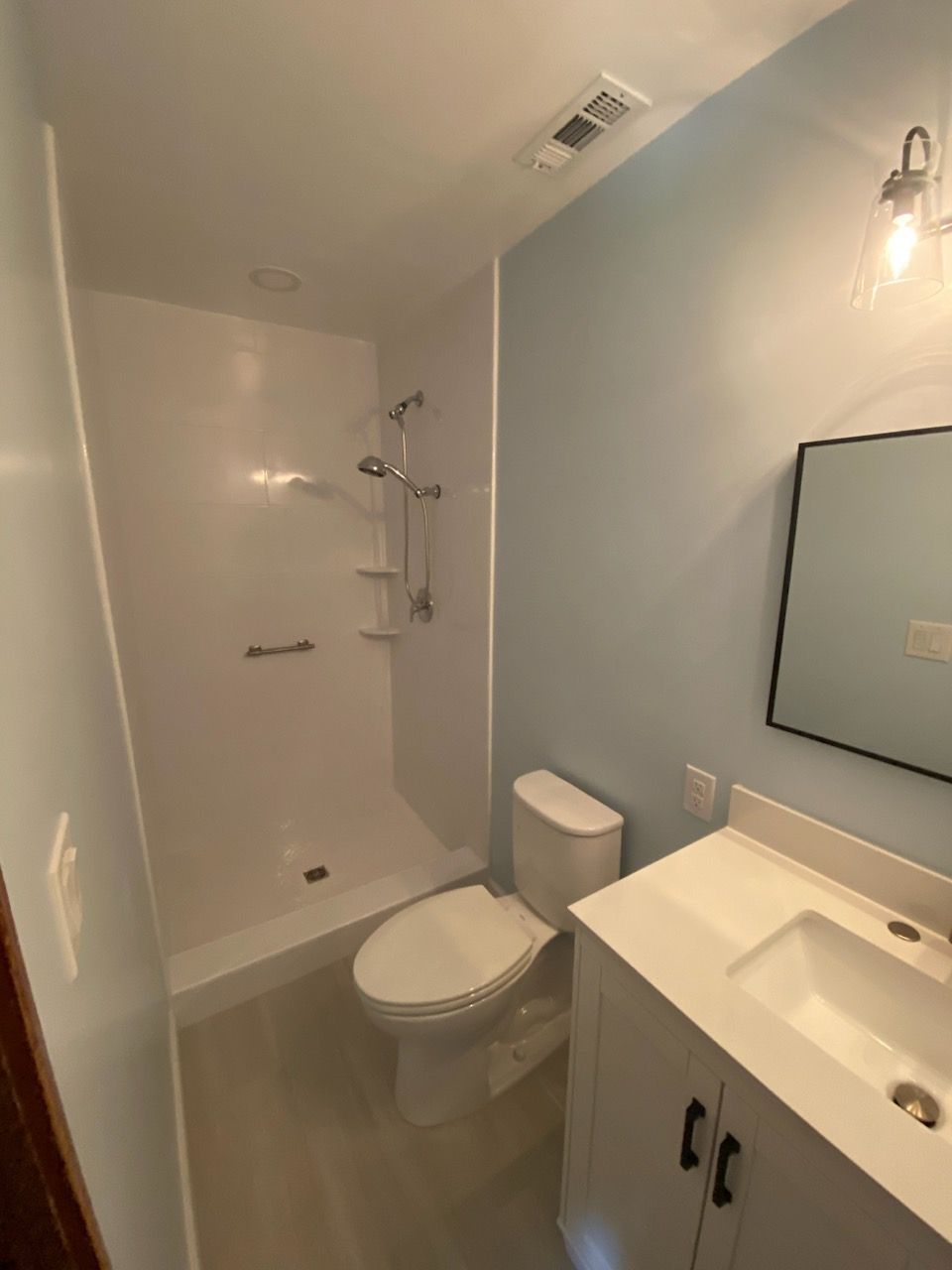 Small bathroom with a white shower, toilet, and vanity with blue walls.