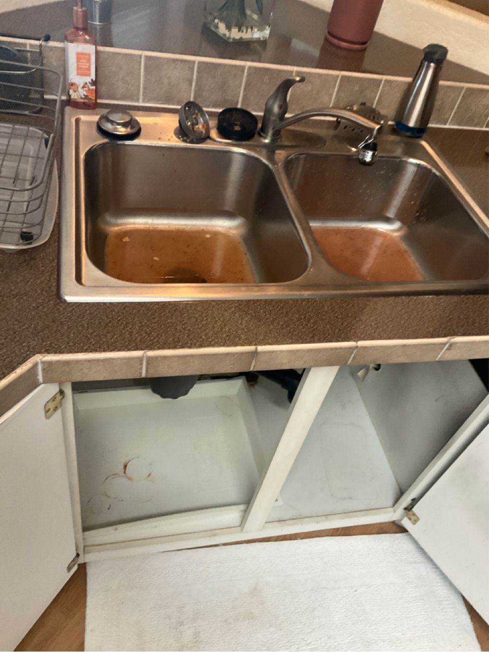Kitchen sink with open cabinet underneath, showcasing rust-colored stains in the basin.