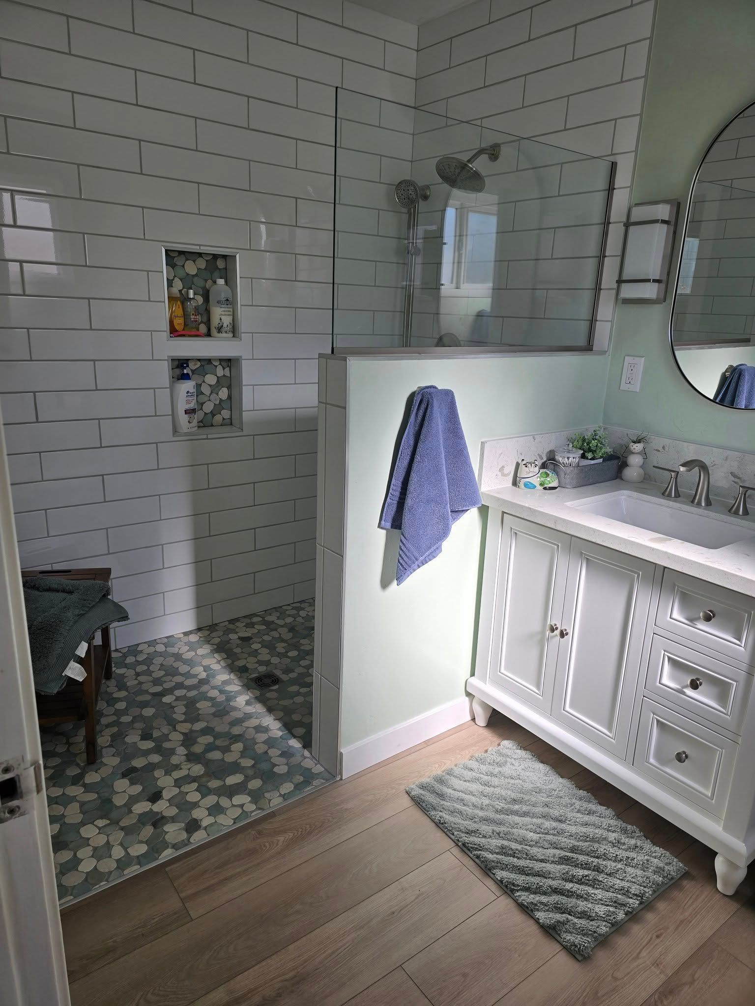 Person working under a kitchen sink. Dark cabinets, stainless steel sink. Tile floor, tools visible.