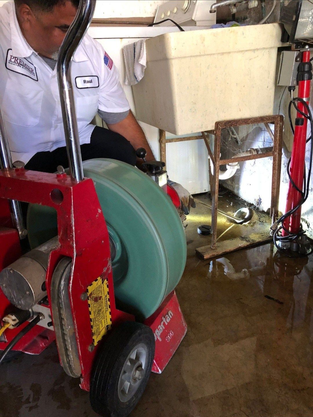 Plumber using a drain cleaning machine in a flooded laundry room.