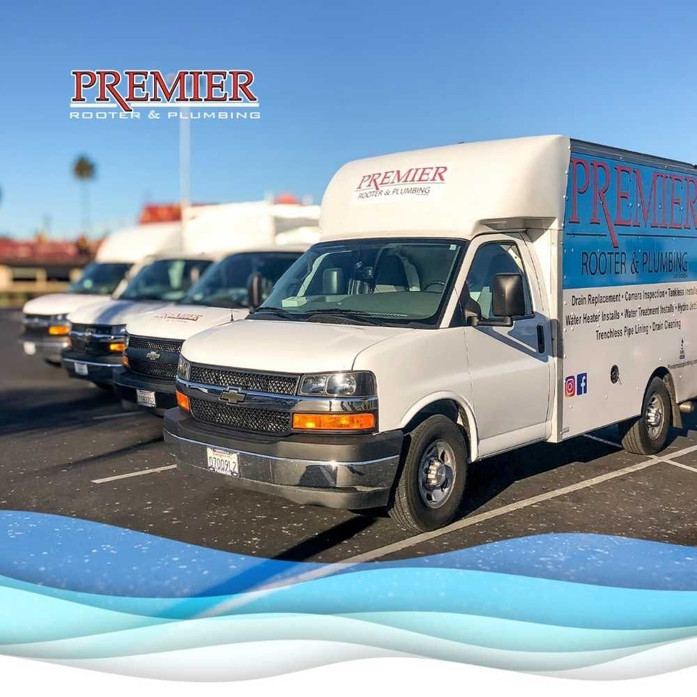 Four white Premier Rooter & Plumbing service vans parked in a lot under a clear blue sky.