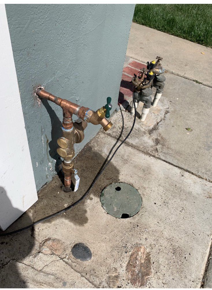 Copper water pipes and sprinkler system components attached to a wall on a concrete surface.