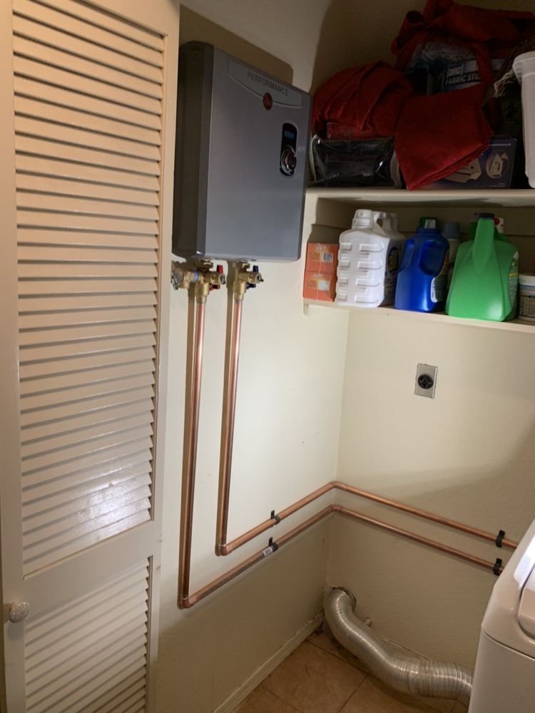 Copper pipes connected to a gray tankless water heater on a wall in a laundry room.
