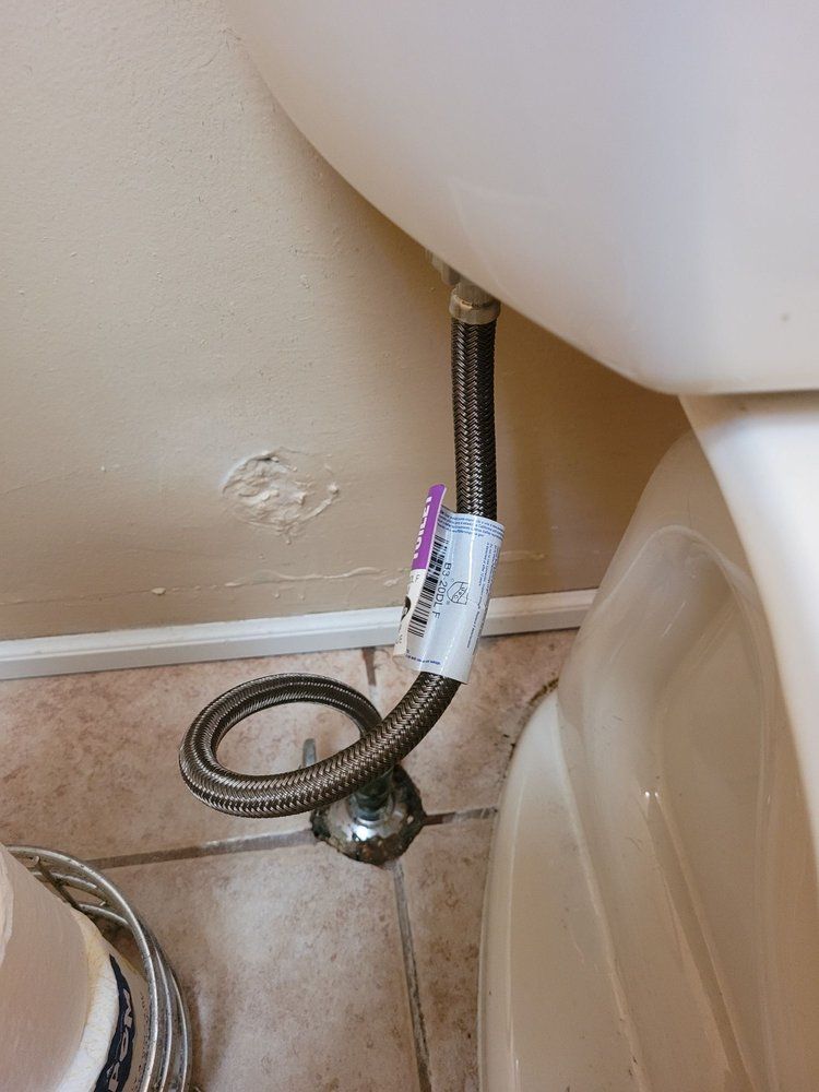 A flexible braided water supply line connected to a toilet, near the wall.