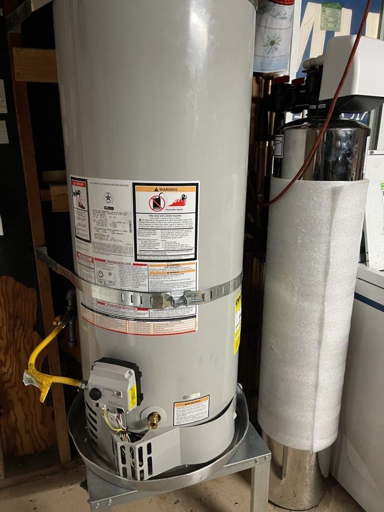 Gray water heater with metal vent pipe. Yellow gas line attached, sitting on a metal stand.