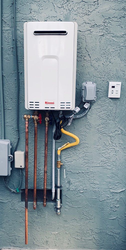 White tankless water heater mounted on a blue stucco wall, with copper pipes and yellow gas line.