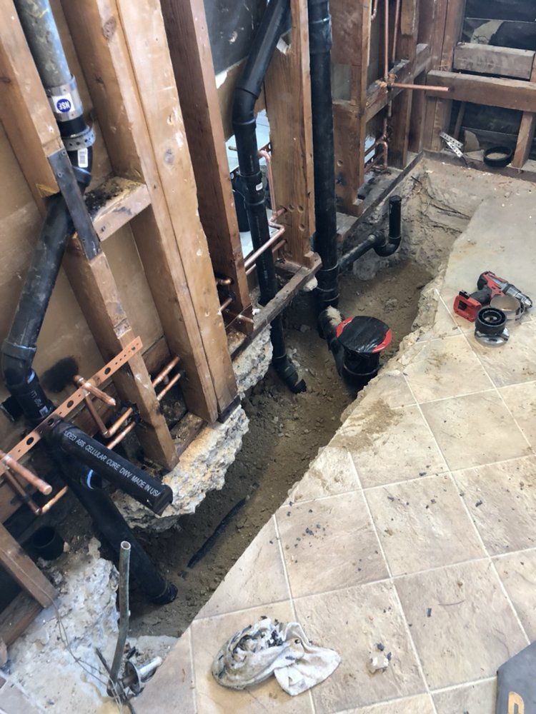 Bathroom renovation: Exposed pipes and plumbing, wood framing, floor tiles, and open trench.