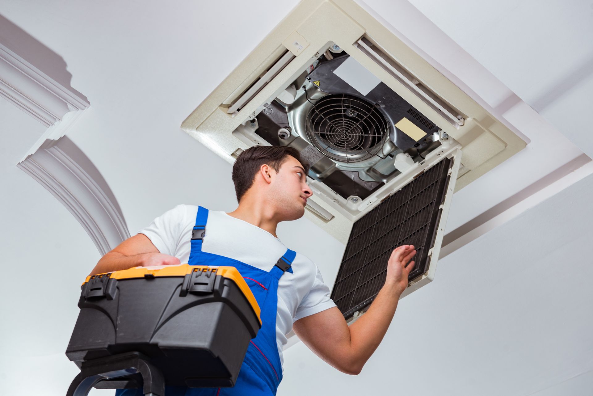 Technician inspecting a ceiling air conditioner while carrying a toolbox and cleaning a filter