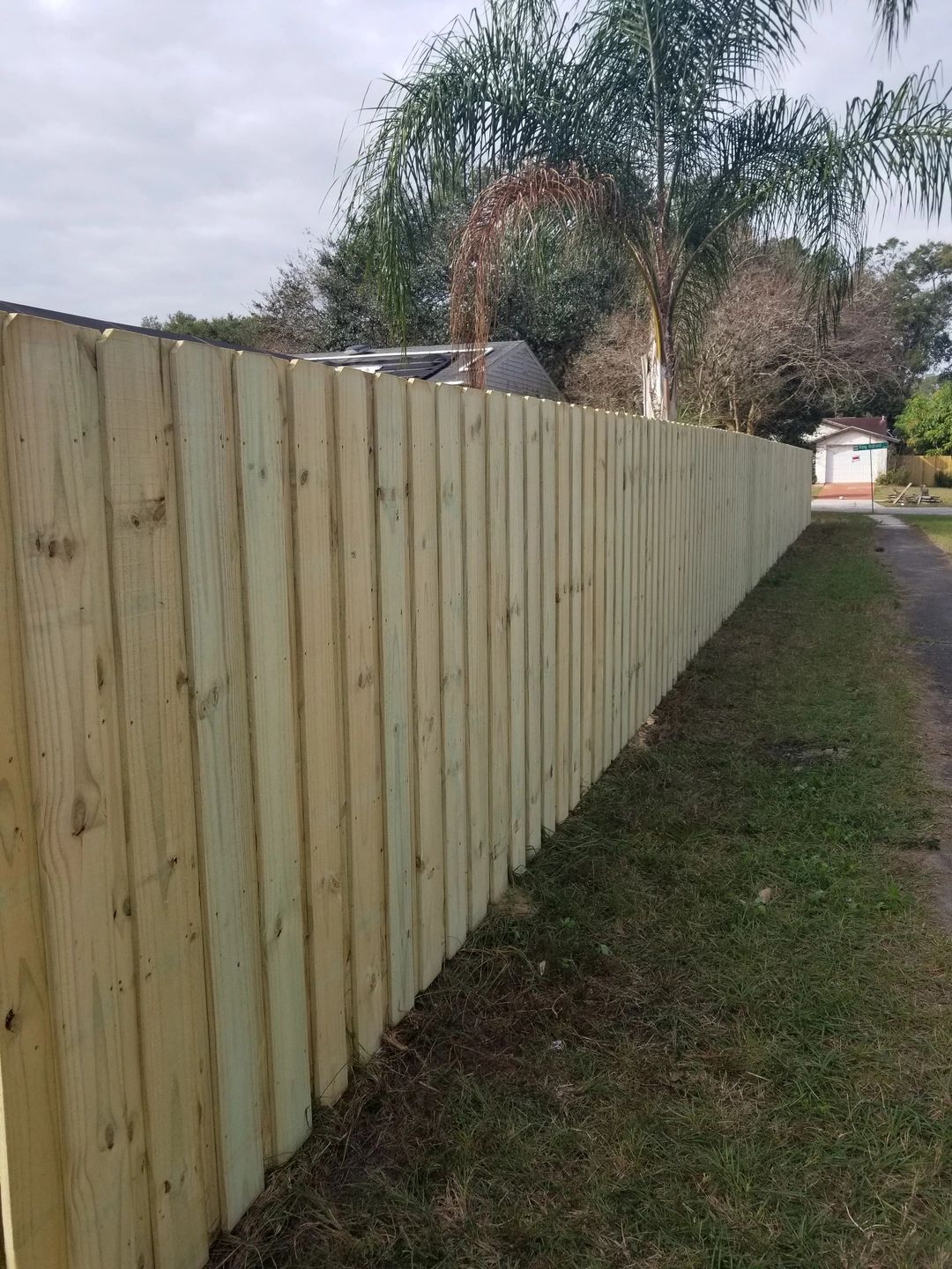 A wooden fence is sitting in the grass next to a dirt road.