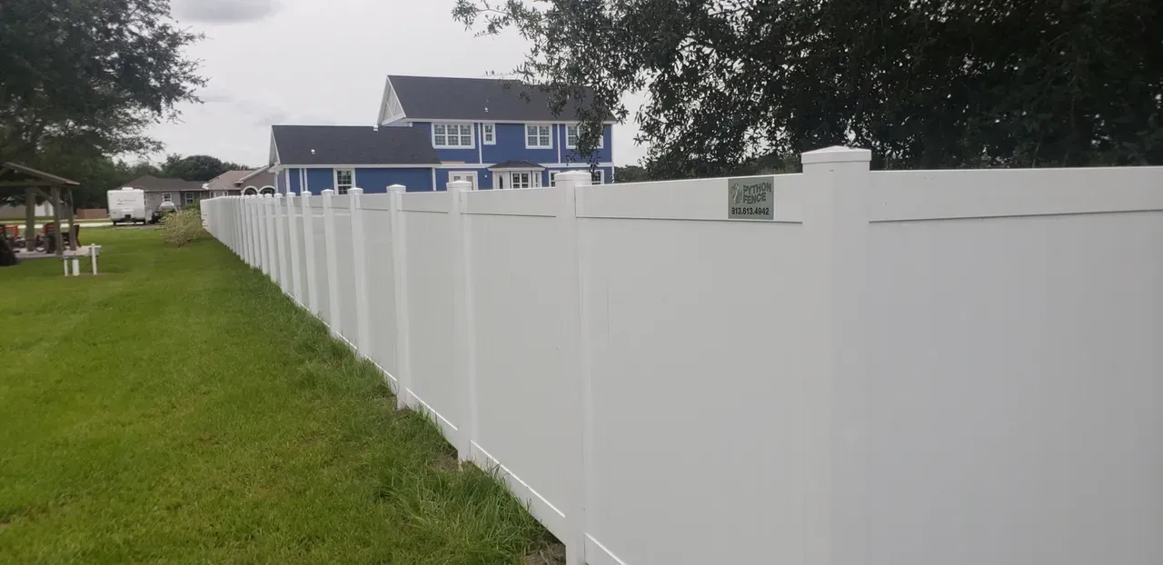A white fence surrounds a lush green yard in front of a blue house.