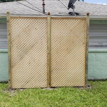 A wooden fence is sitting in front of a house with a satellite dish on the roof.